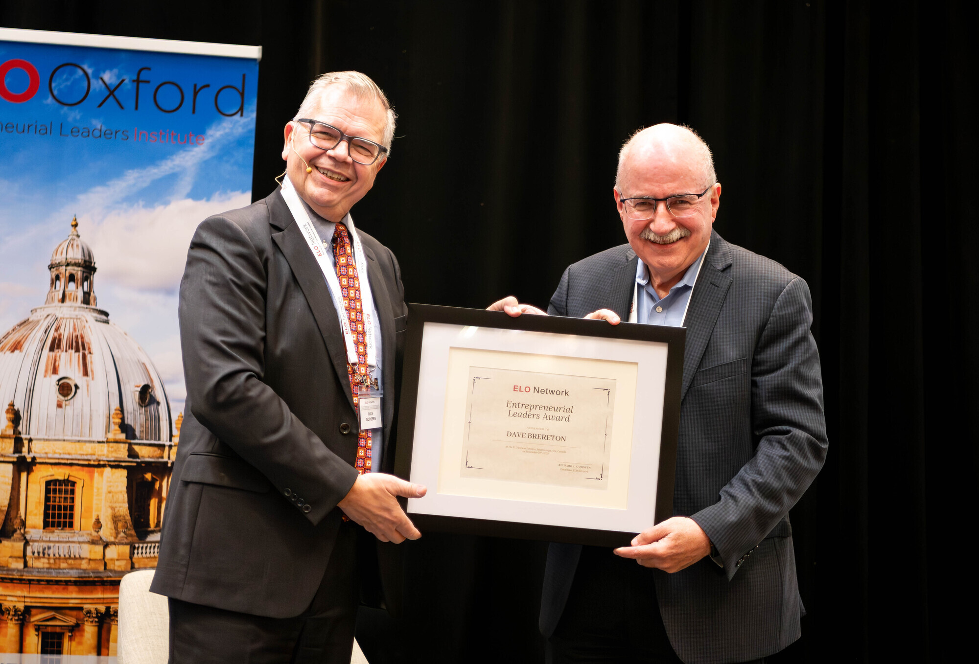 Rick Goossen presenting an award in a picture frame to Dave Brereton on stage